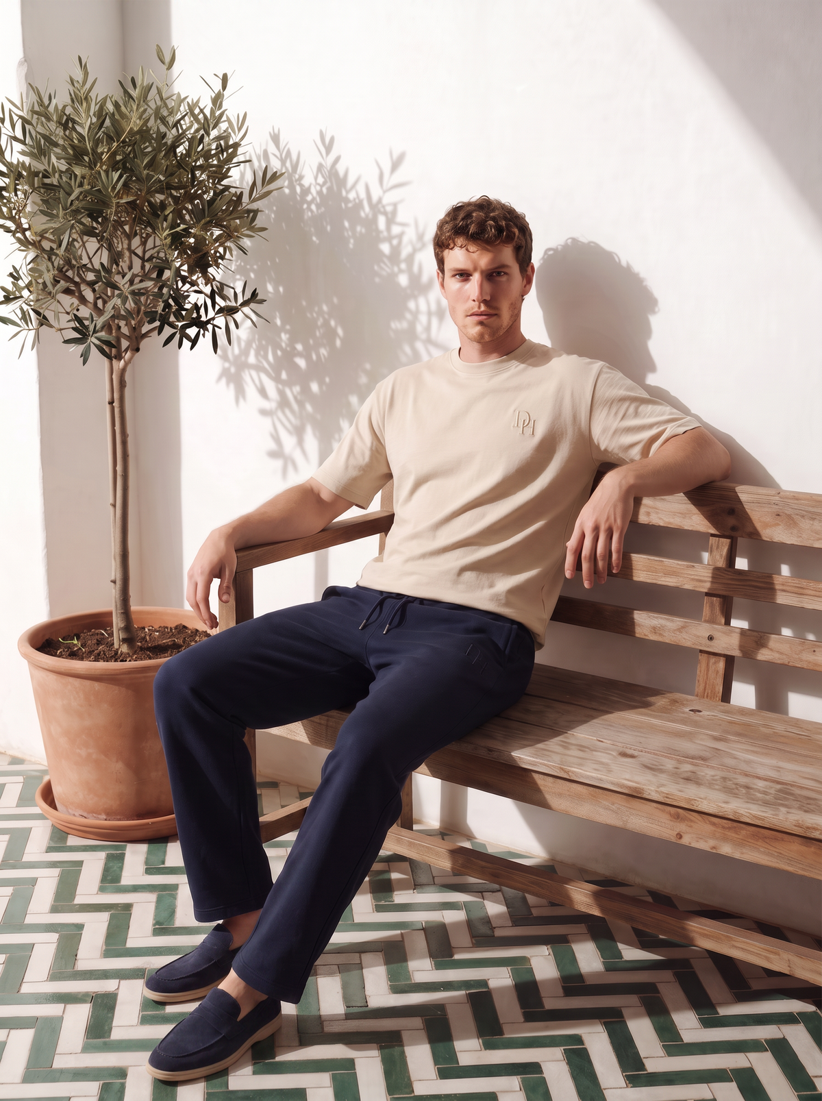 Model wearing the Warm Bone Foundation Heavyweight T-Shirt and Midnight Navy Refined Straight-Leg Sweatpant seated beside an olive tree