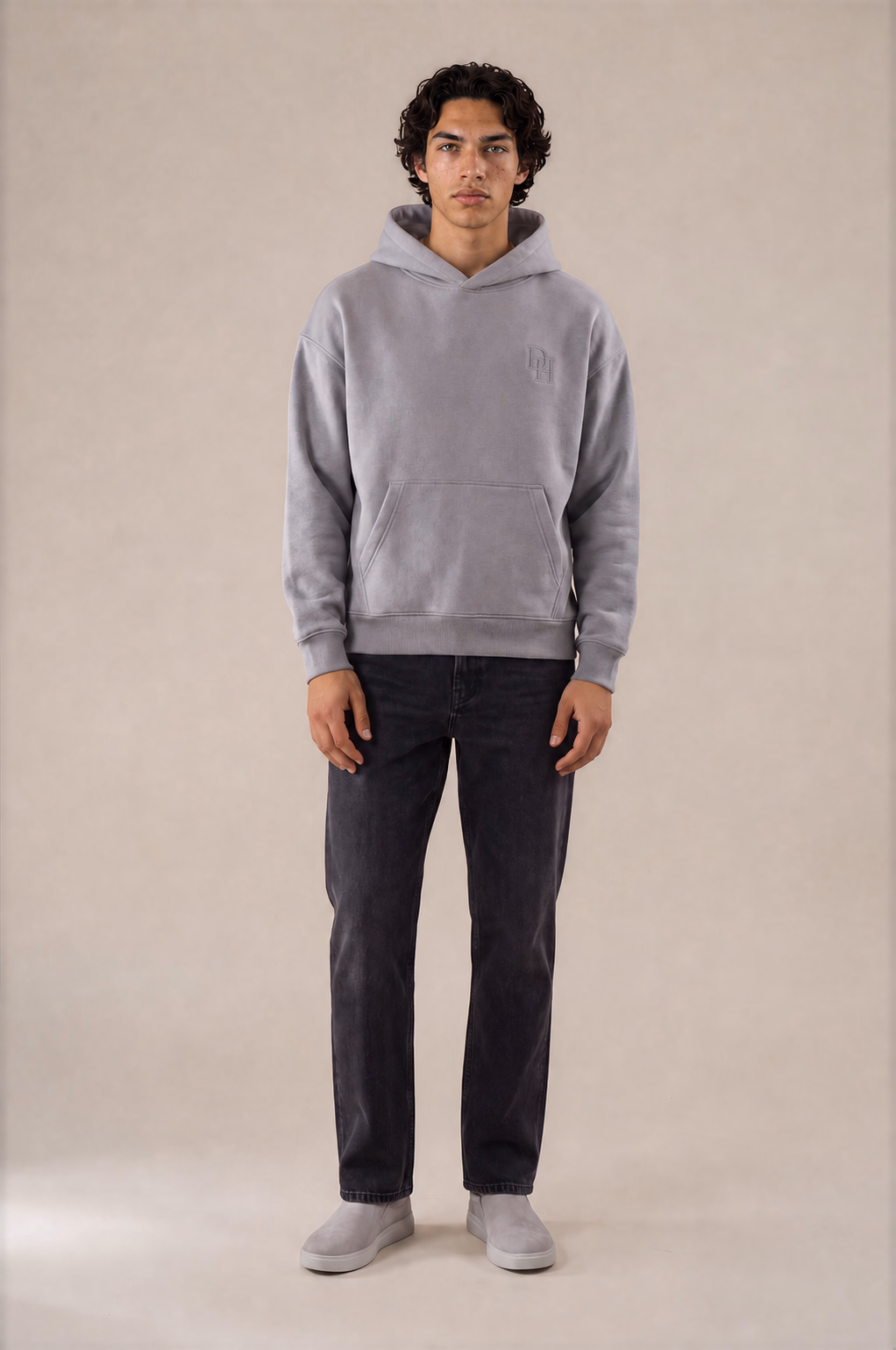 Full-body view of a model wearing the stringless light heather Dynast Heir hoodie with tonal wearer-left chest embroidery
